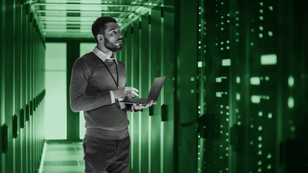 It,Technician,Works,On,Laptop,Next,To,A,Server,Cabinet